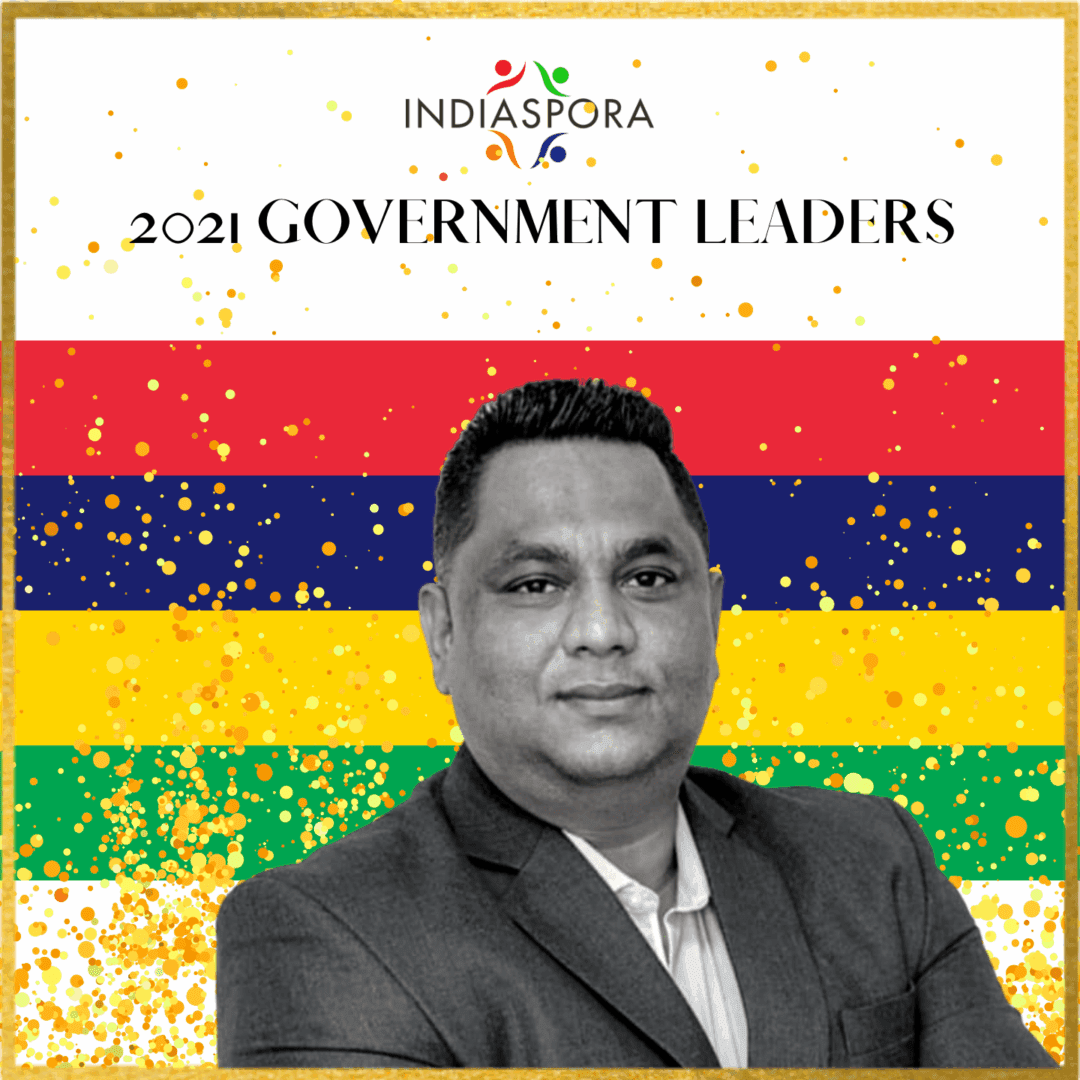 A man in suit and tie standing next to the flag of mauritius.