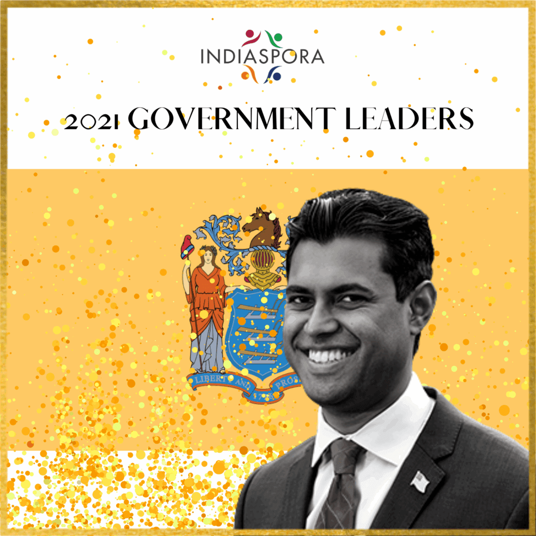 A man in a suit and tie standing next to the state flag.